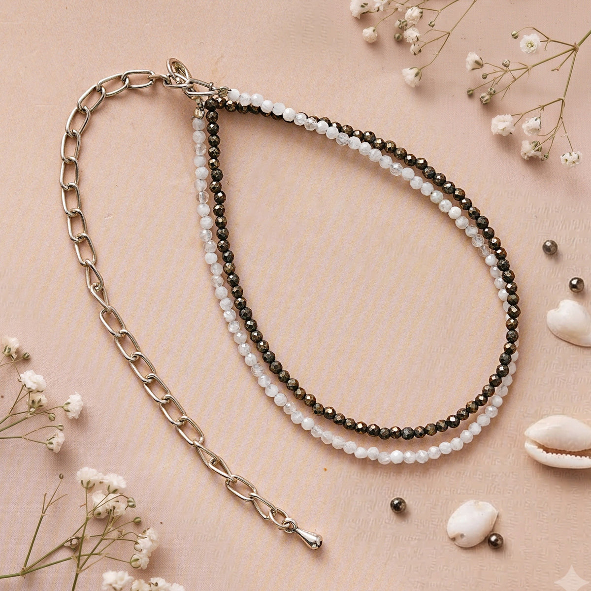 Pyrite and quartz anklet with its silver-toned chain on a blush background with shells and dried flowers
