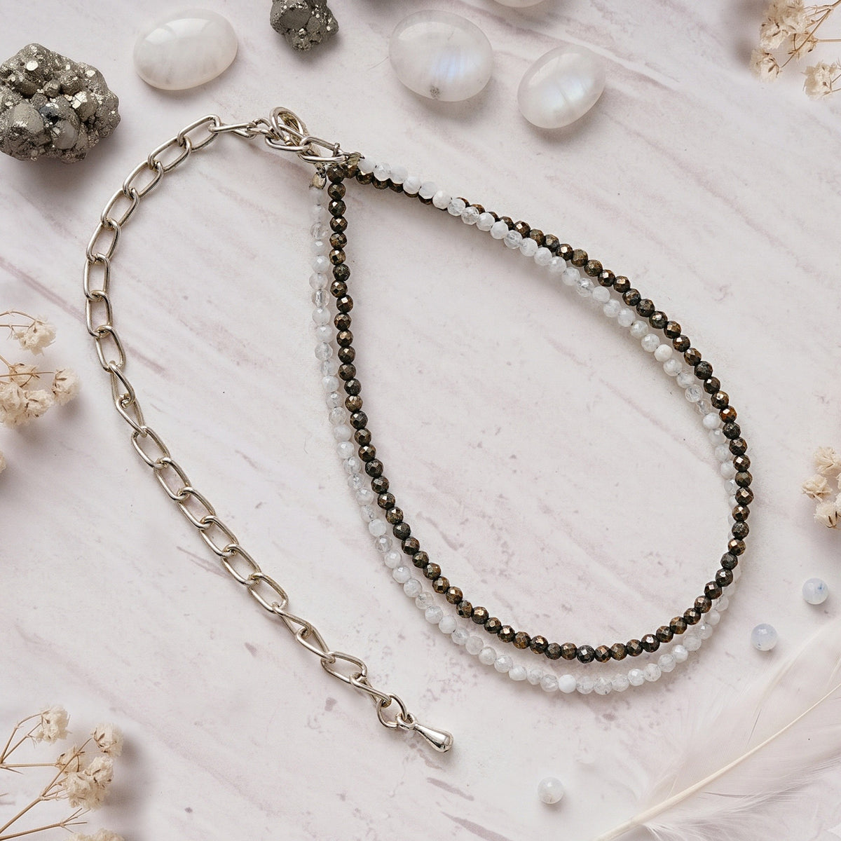 Pyrite and quartz anklet on white marble beside raw pyrite and polished stones