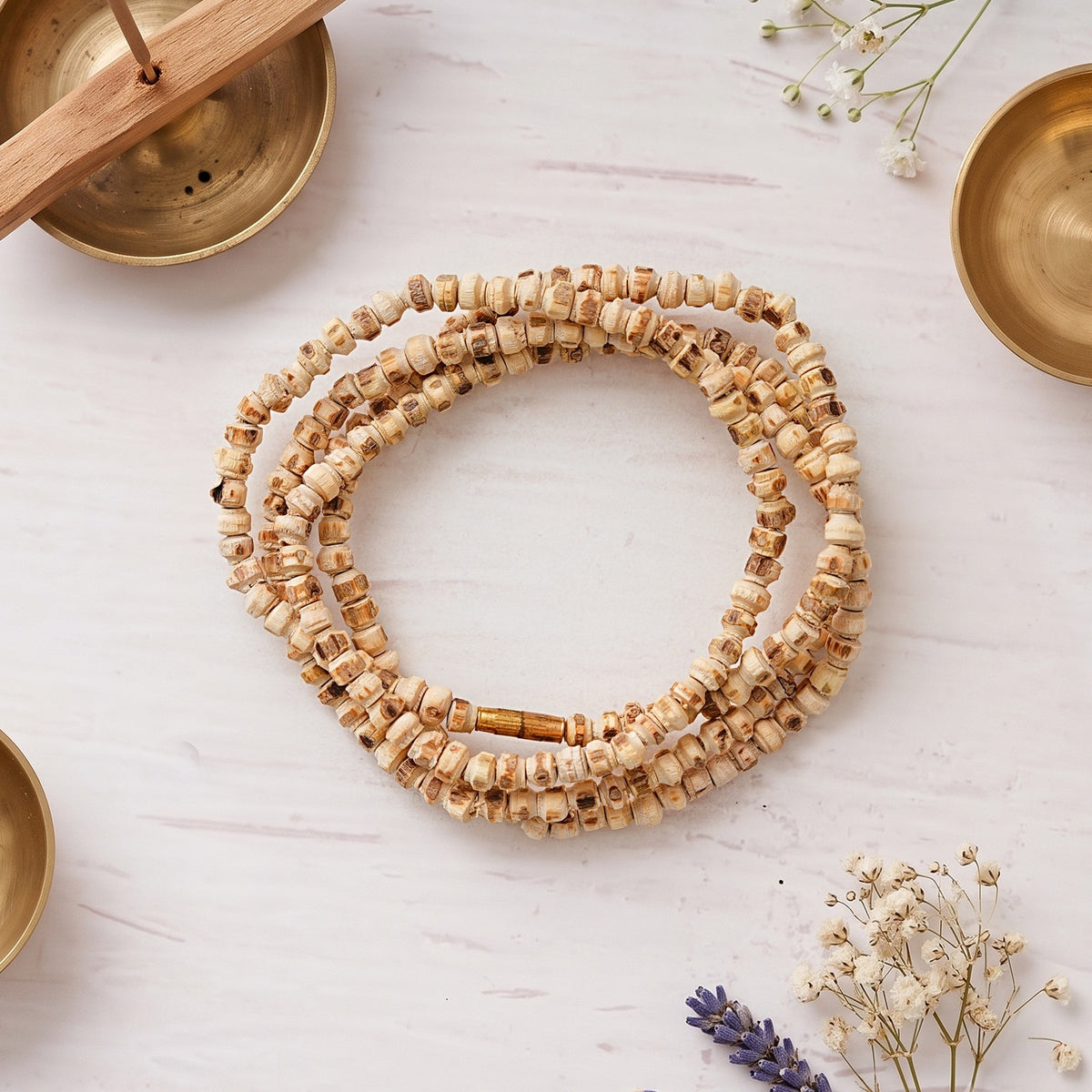 Tulsi Kanthi Mala coiled on a marble surface with brass bowls