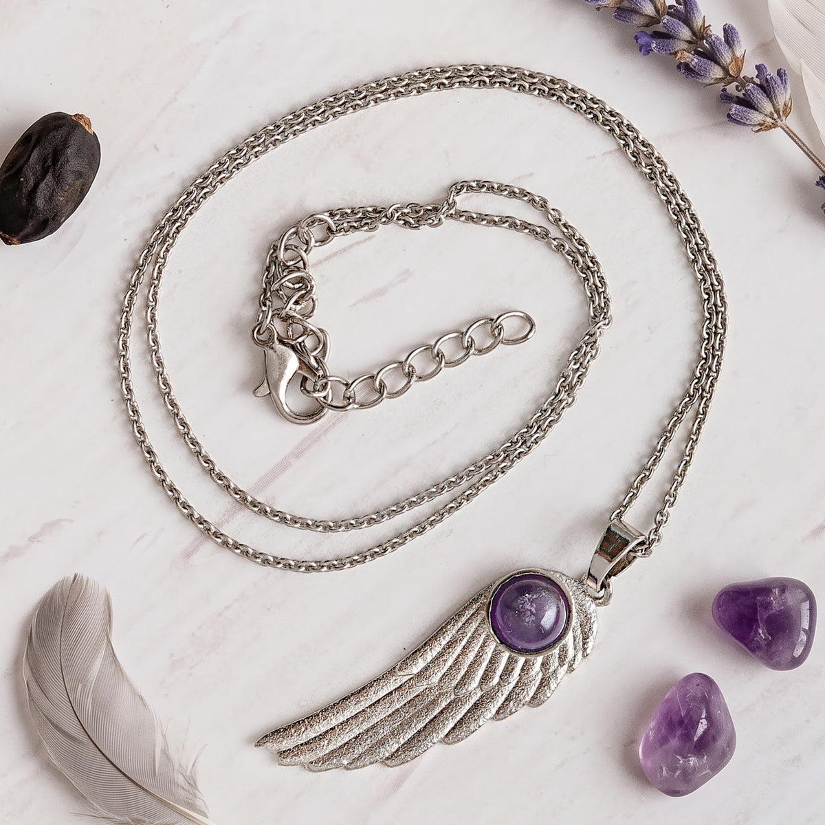 Amethyst feather pendant on white marble with raw amethyst, a grey feather and lavender