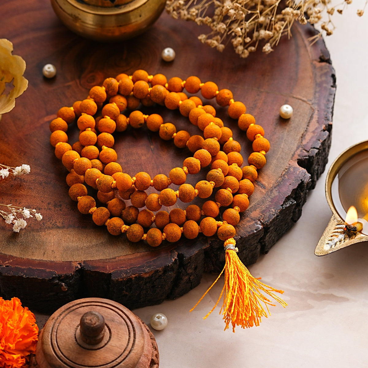 Haldi Jaap Mala coiled on a wooden slab beside a brass diya and pearls