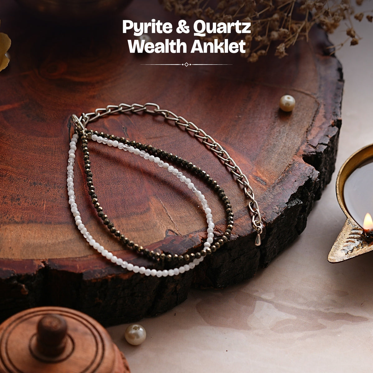 Pyrite and quartz double-strand anklet on a wooden slab beside a lit diya
