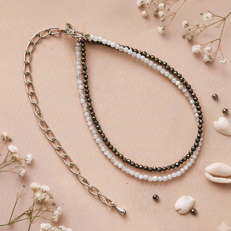 Pyrite and quartz anklet with its silver-toned chain on a blush background with shells and dried flowers