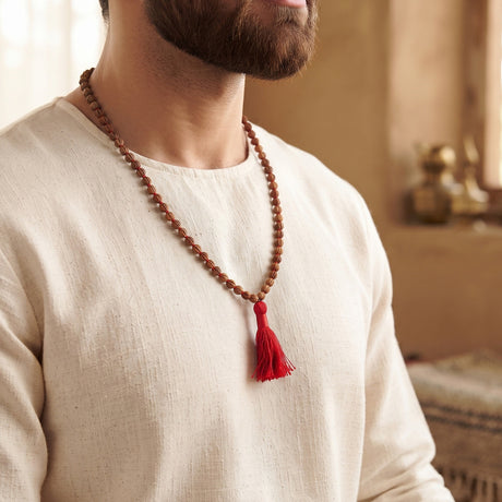 Man wearing the Chandan Carved Bead Mala with its red tassel over a cream kurta