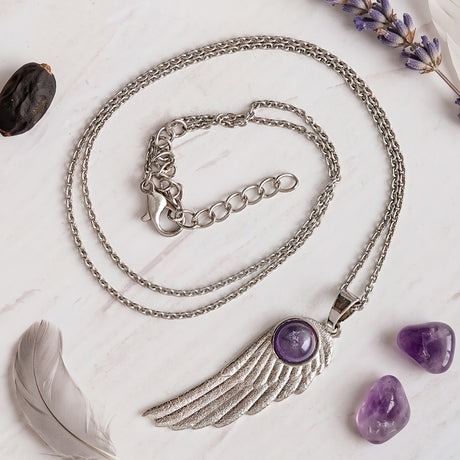 Amethyst feather pendant on white marble with raw amethyst, a grey feather and lavender
